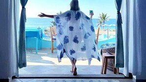 A room with a view of the beach, a person standing by the window, and a table with a chair. - Villa Star of the Sea - Adults Only (Isla Navidad)