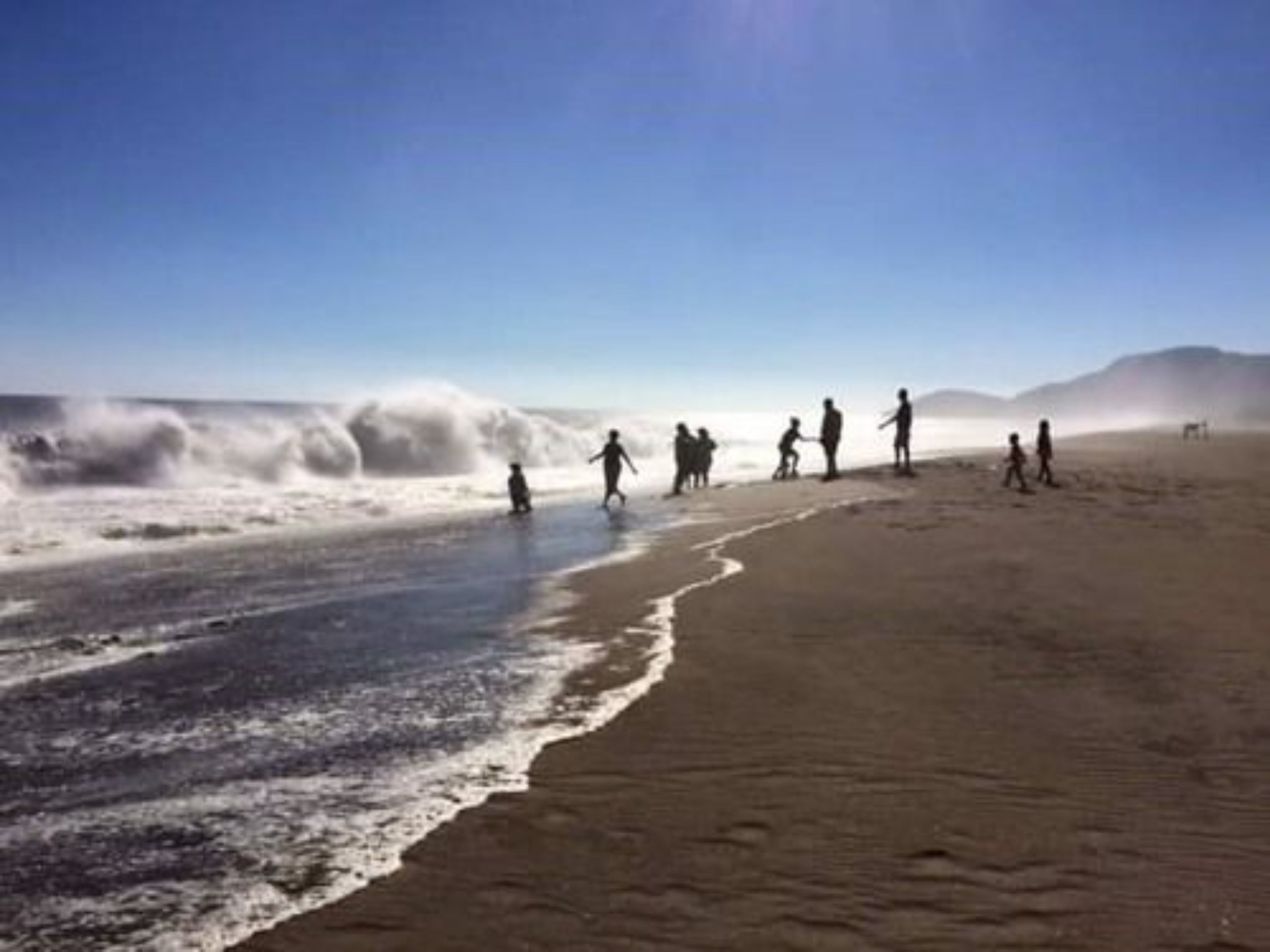 A beach with people walking along the shore.