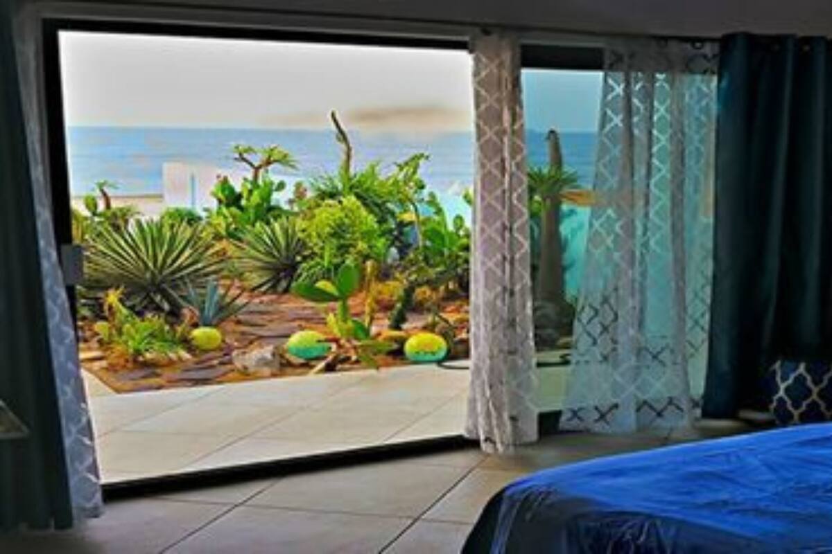 Een kamer met een bed, een stoel en uitzicht op de oceaan door een schuifdeur.