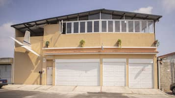 A two-story building with a flat roof, two garage doors, and a small balcony with potted plants.