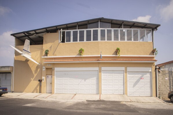 A two-story building with a flat roof, two garage doors, and a small balcony with potted plants. - Euro Hostal - Hostel (Guatemala City)