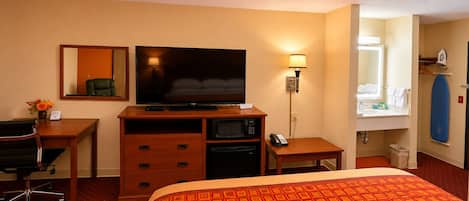 A hotel room with a bed, a desk with a chair, a television, a microwave, a telephone, a mirror, and a bathroom.