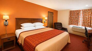 A hotel room with a large bed, bedside lamps, a chair, an air conditioning unit, and a door.