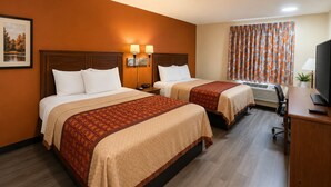 A hotel room with two beds, a desk with a TV, and a window with curtains.
