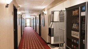 A hotel hallway with a red carpet, vending machines, and a refrigerator.
