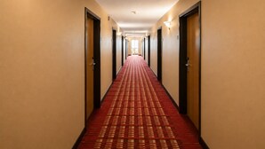 A hotel hallway with carpeted floors, doors on both sides, and wall-mounted lights.