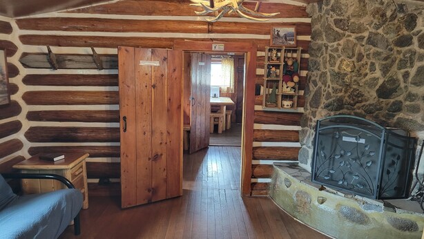 A log cabin interior with a wooden floor, a sofa, a fireplace, and a stone wall. - Chinook Cabins & RV Park (South Fork)