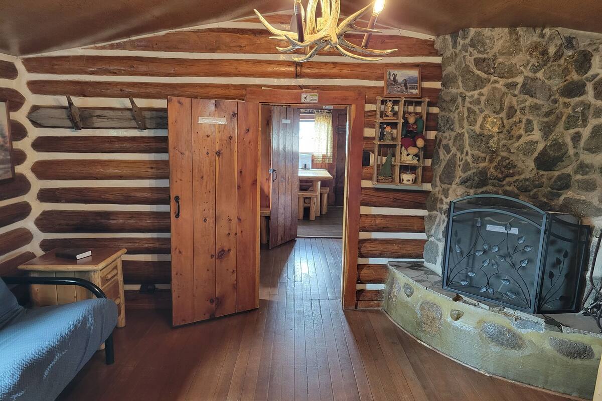 L’intérieur d’une cabane en rondins, avec un plancher en bois, un canapé, une cheminée et un mur en pierre.