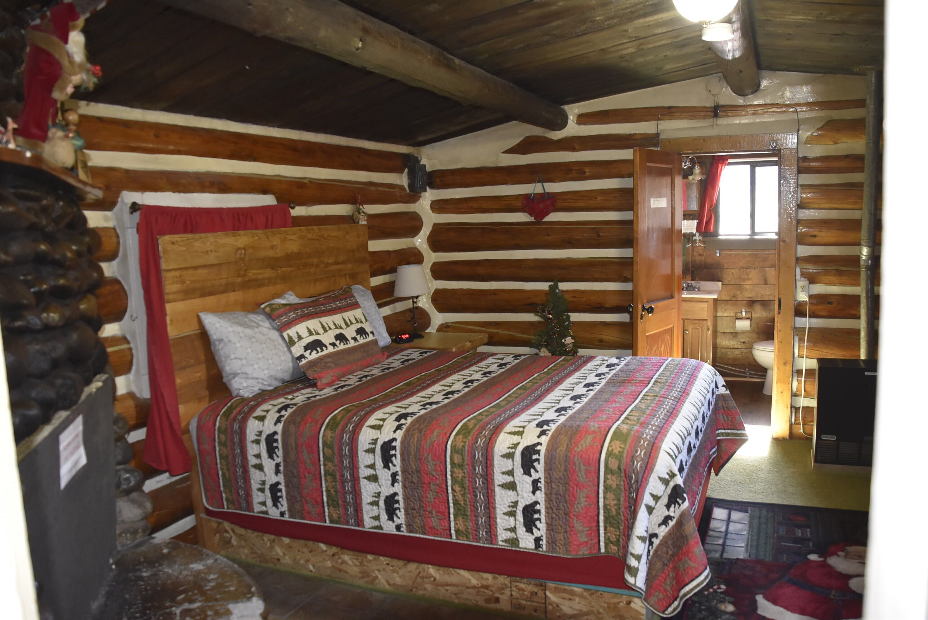 A log cabin bedroom with a wooden bed, a nightstand, a dresser, and a window with curtains.
