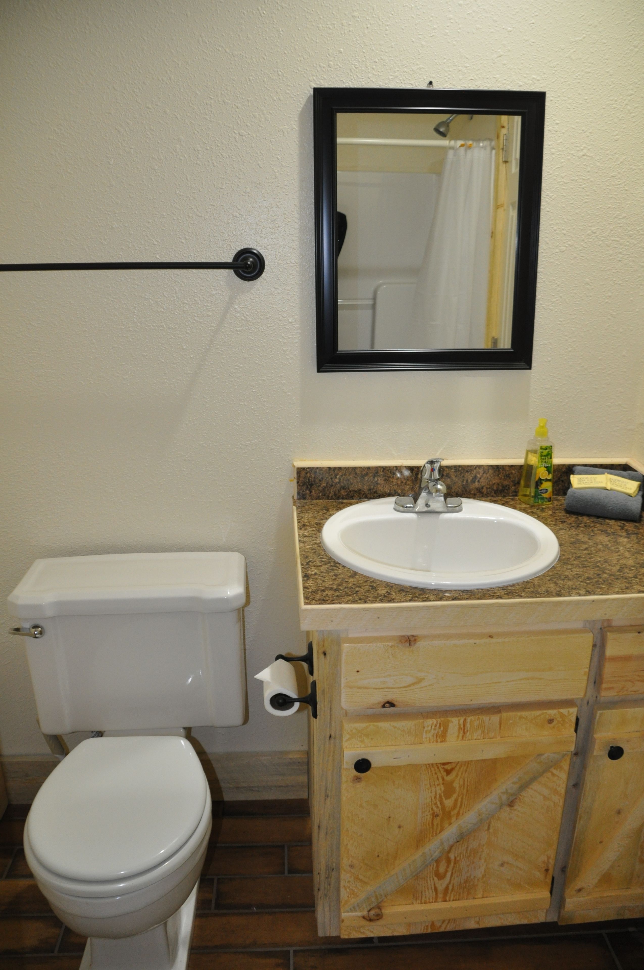 A bathroom with a toilet, sink, mirror, and wooden cabinet.