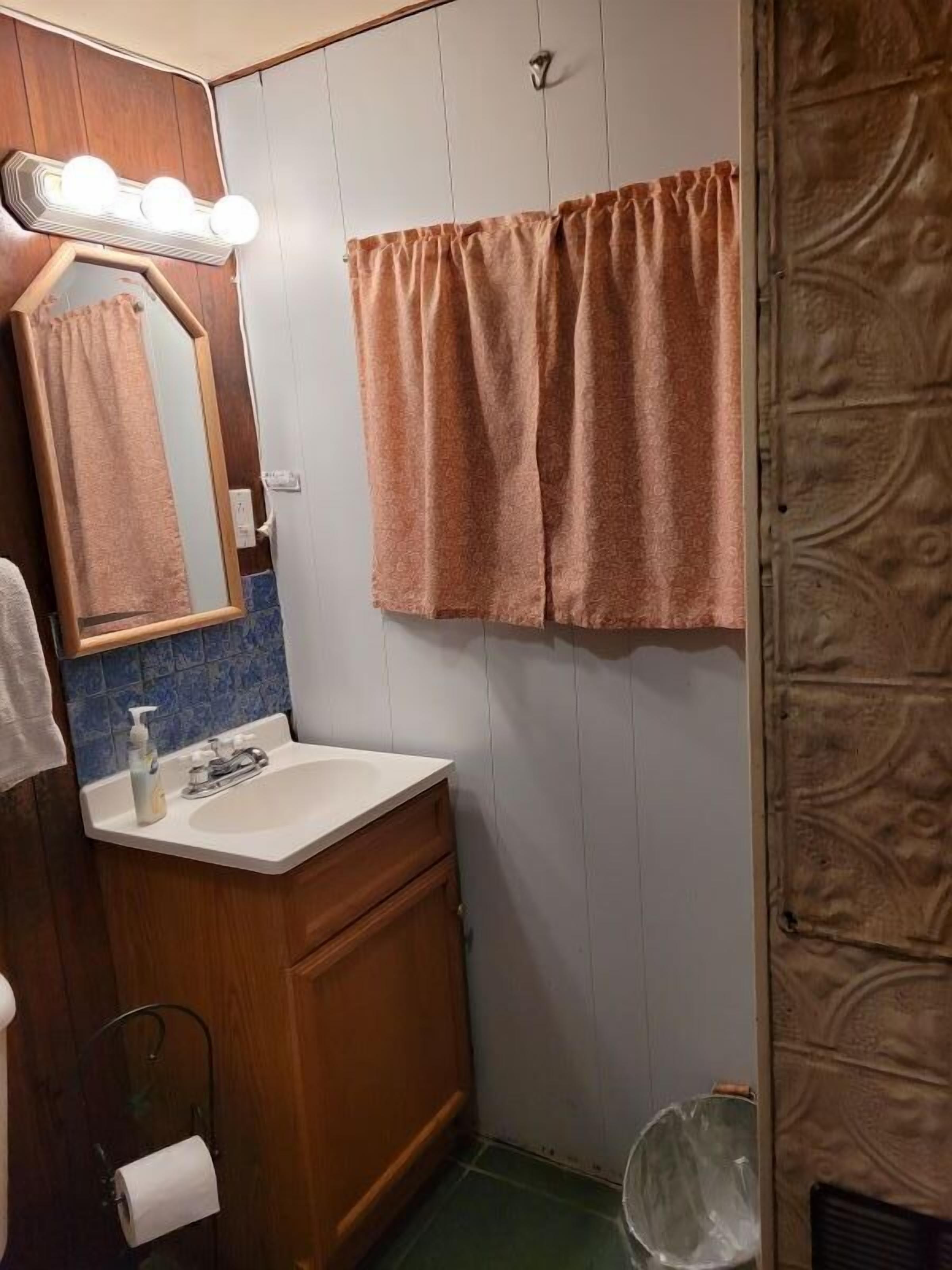 Ein Badezimmer mit einem Holzkonsolenunterschrank, einem weißen Waschbecken, einem beleuchteten Spiegel und einem Handtuch an der Wand.