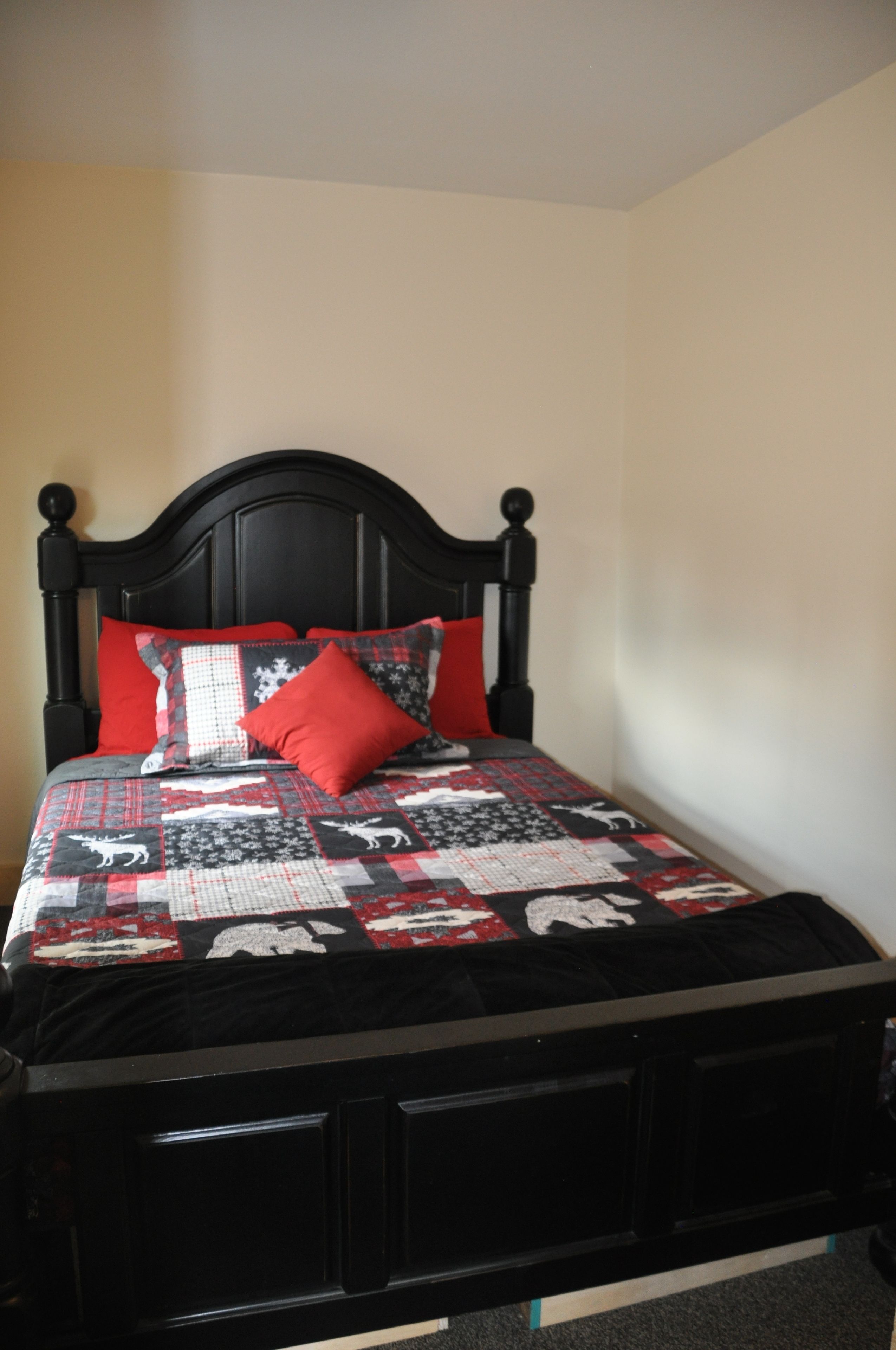 A bed with a black frame, red and white bedding, and a quilt with animal patterns.