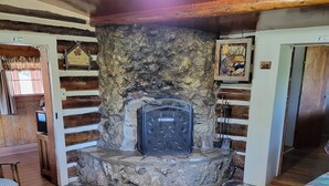 A cozy room with a stone fireplace, wooden floors, and a bed with a colorful quilt. - Chinook Cabins & RV Park (South Fork)