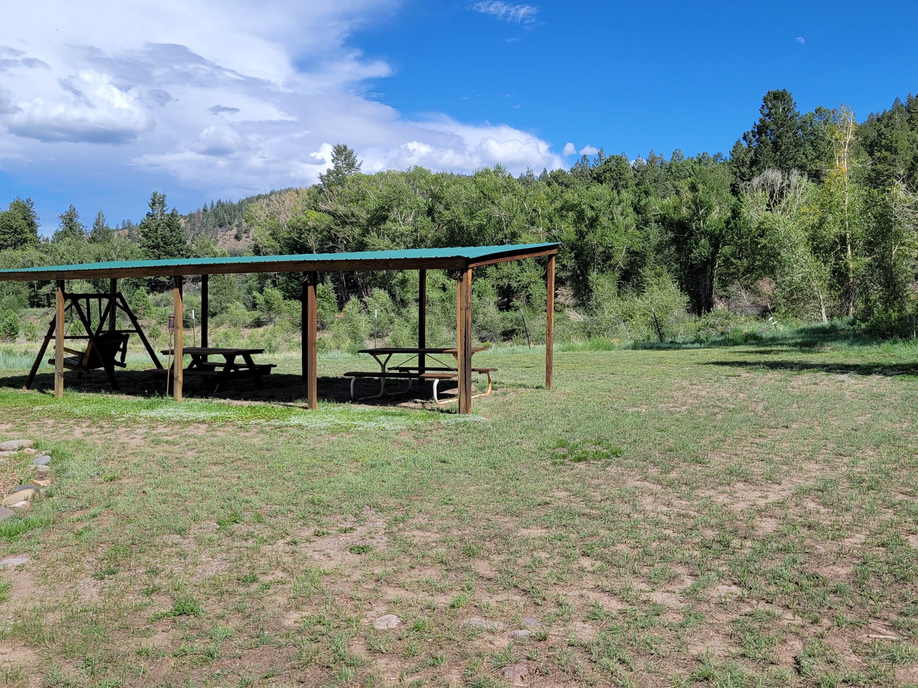 A picnic area with a covered shelter and picnic tables in a grassy field.