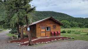 A rustic cabin named 'Fort Wilderness' with a wooden exterior, a porch with red chairs, and a gravel driveway. - Chinook Cabins & RV Park (South Fork)