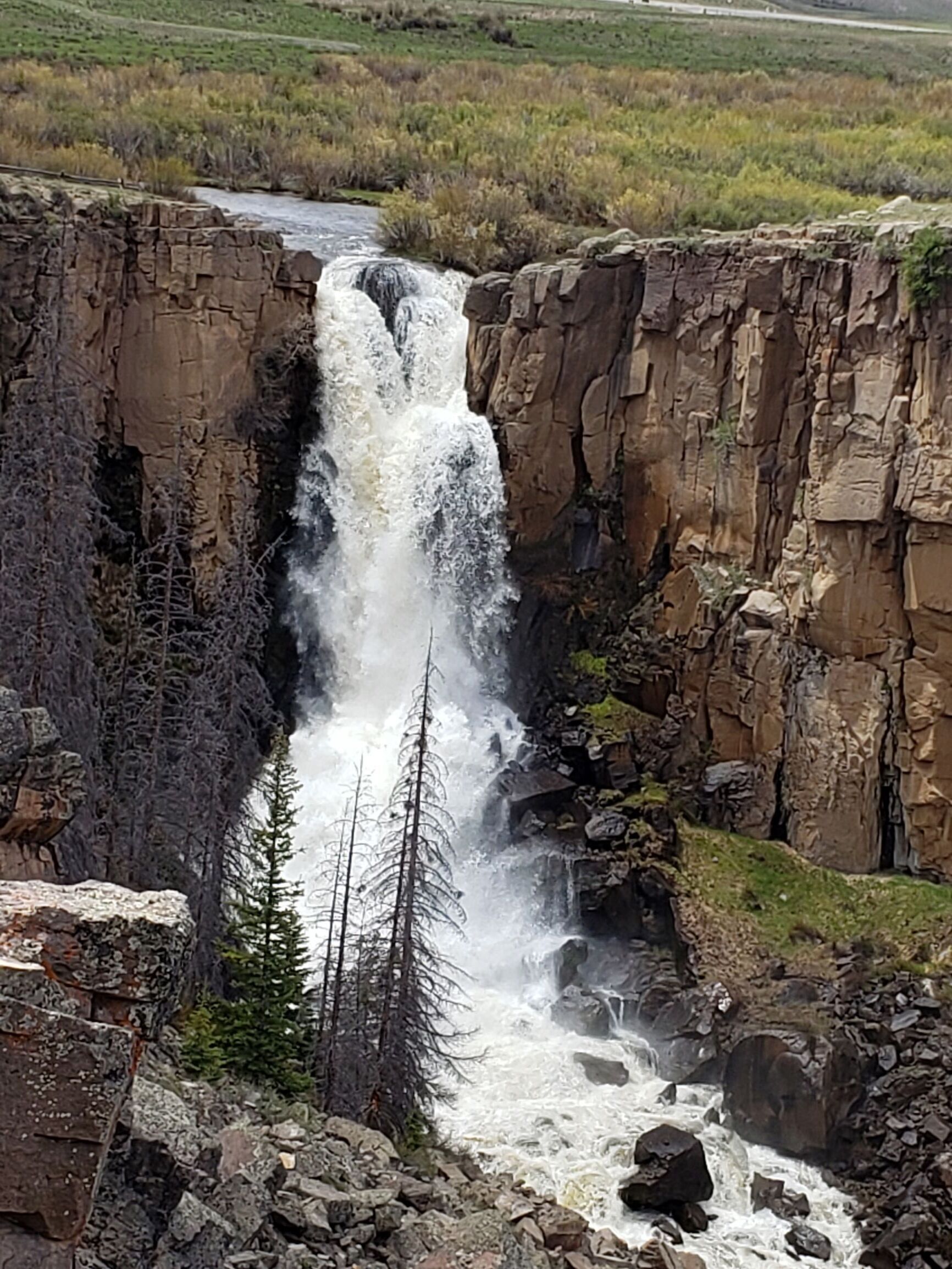 A waterfall cascading down a rocky cliff surrounded by sparse vegetation.