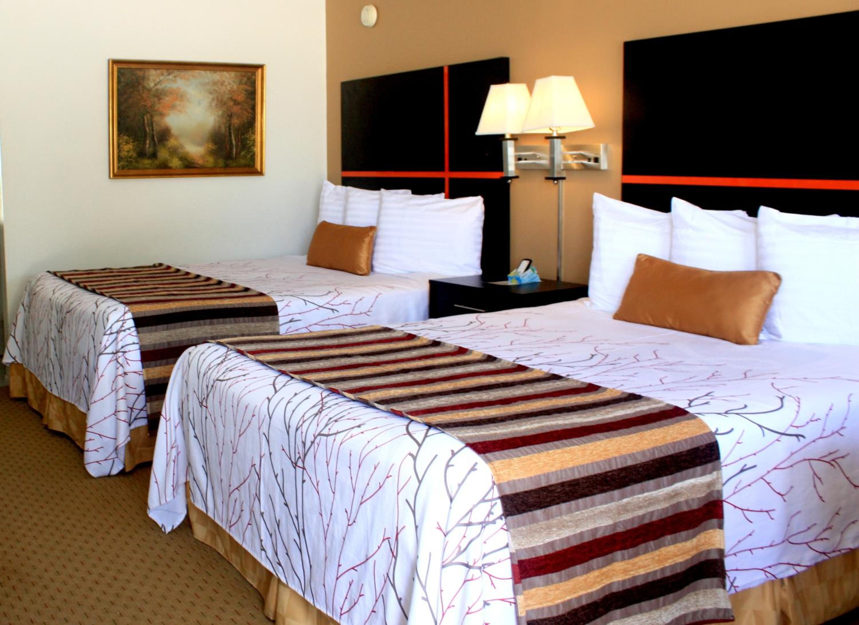 Une chambre d’hôtel avec deux lits, un tableau au mur, une table de chevet avec une lampe et un mur d’accent rouge.