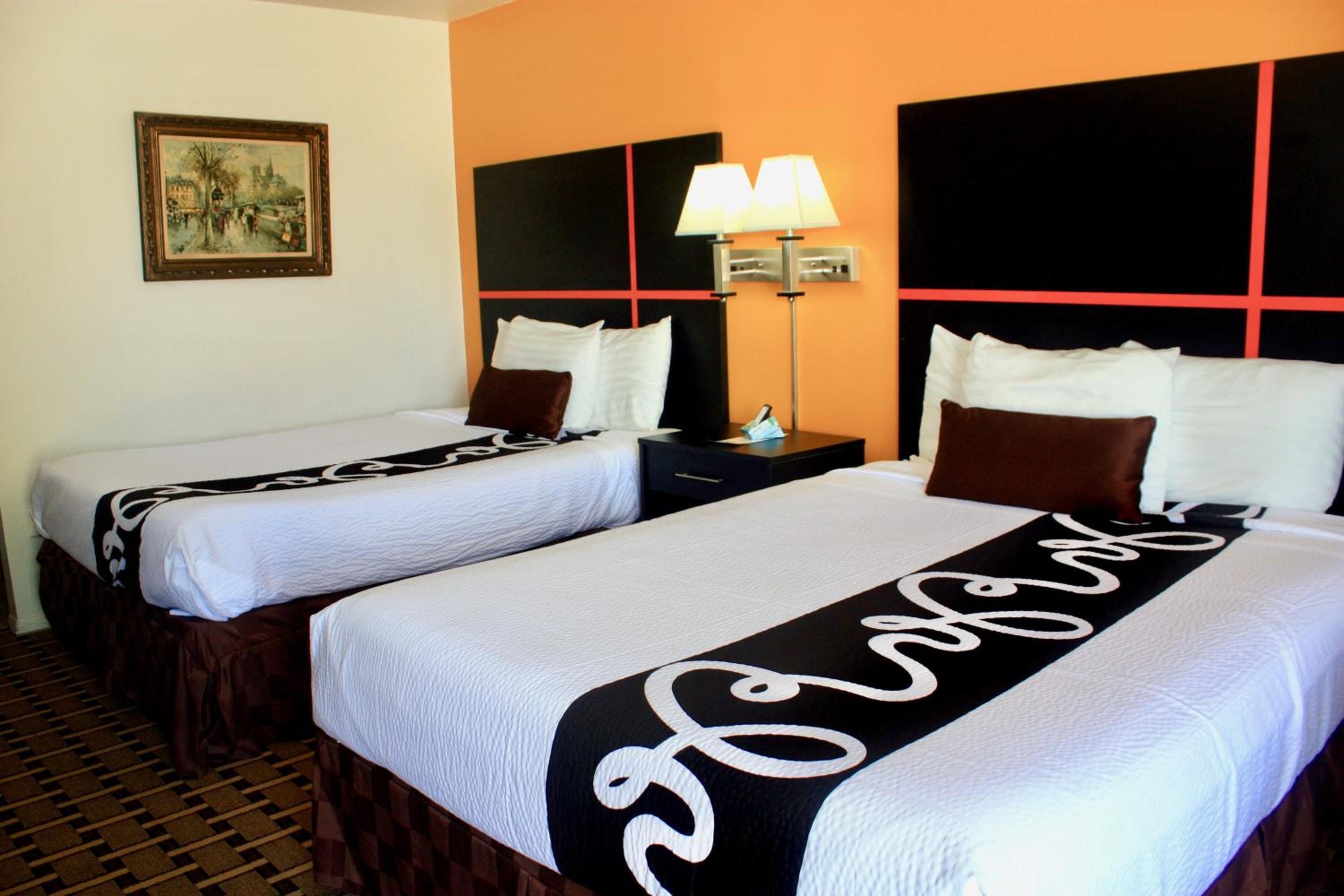 Habitación de hotel con dos camas, una mesita de noche, una lámpara y un cuadro en la pared.