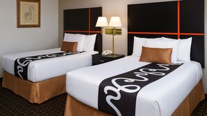 Two twin beds with white bedding and brown headboards, a nightstand with a lamp, and a framed picture on the wall. - Chaparral Motor Inn (Burlington)