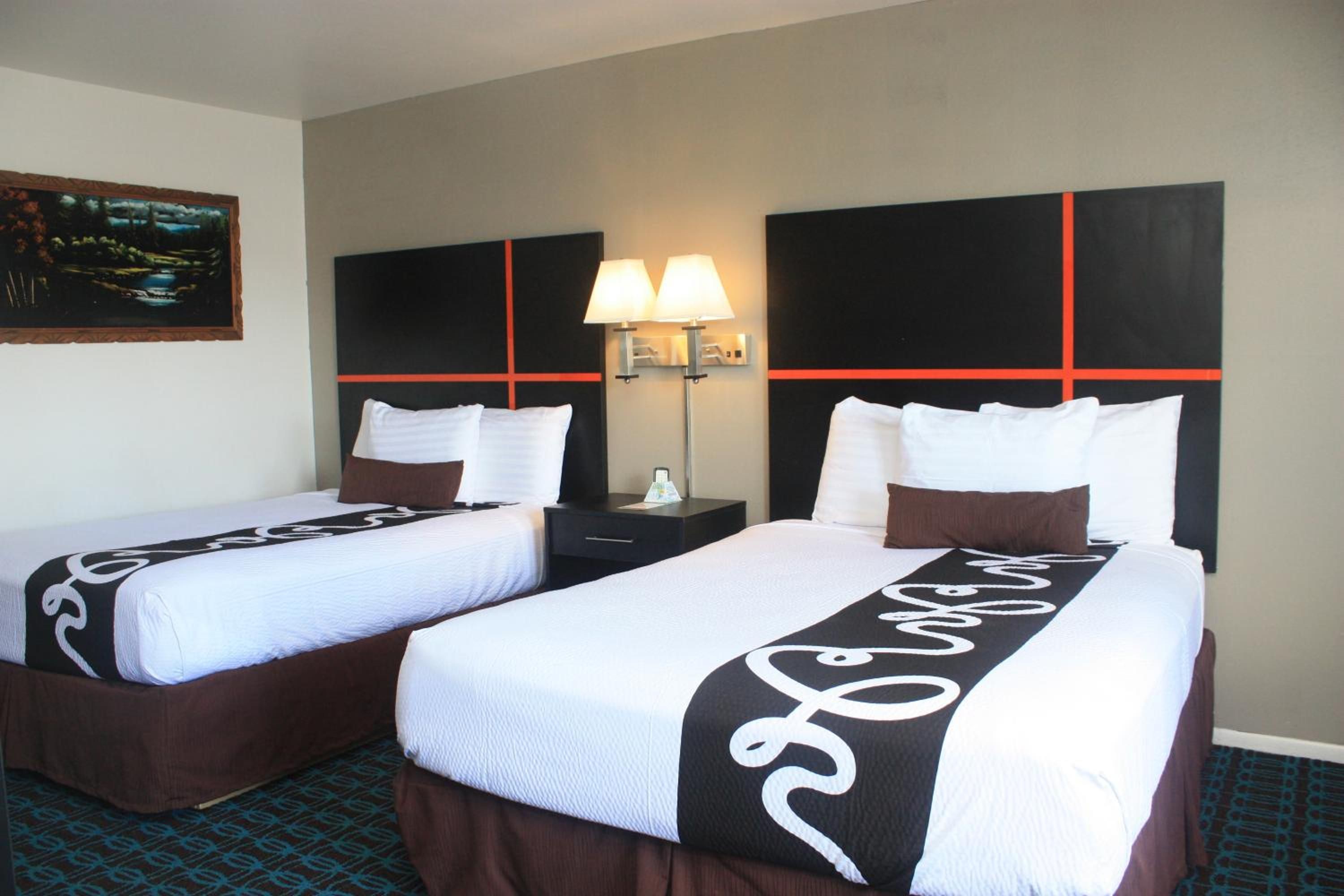 Habitación de hotel con dos camas, una mesita de noche, una lámpara y un cuadro en la pared.