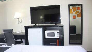 Habitación de hotel con cama, escritorio, silla, televisor, microondas y espejo.