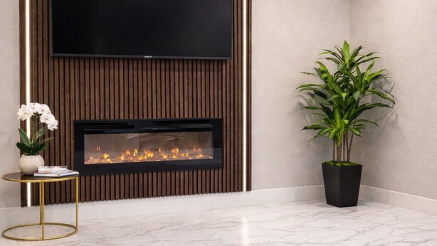 A modern living room with a flat-screen TV mounted above a fireplace, a potted plant, and a grey sofa. - Chaparral Motor Inn (Burlington)