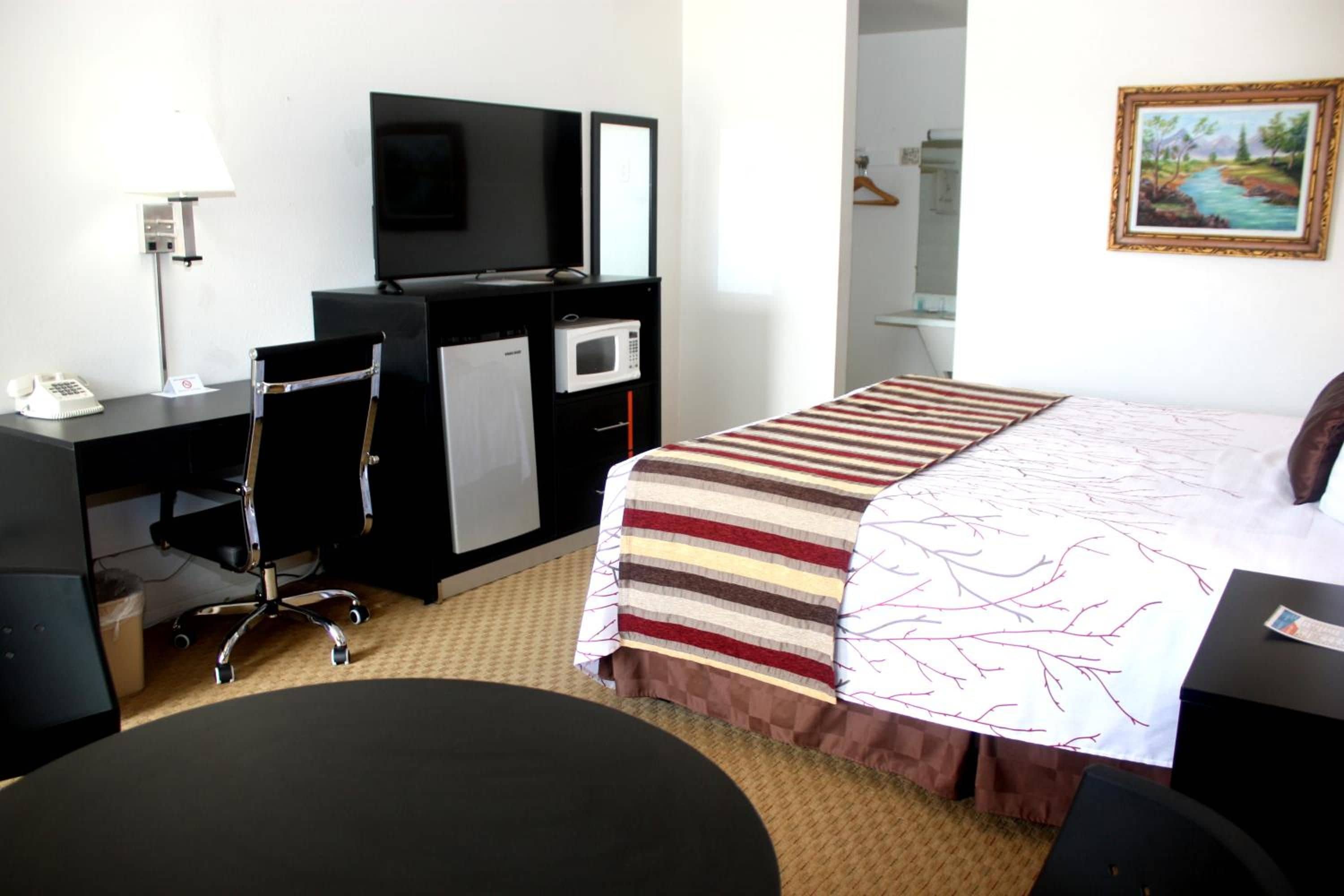 Une chambre d’hôtel équipée d’un lit, d’un bureau, d’une chaise, d’une télévision, d’un four à micro-ondes et d’un tableau au mur.