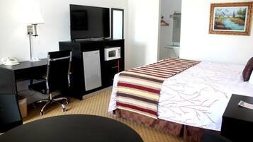 Une chambre d’hôtel équipée d’un lit, d’un bureau, d’une chaise, d’une télévision, d’un four à micro-ondes et d’un tableau au mur.