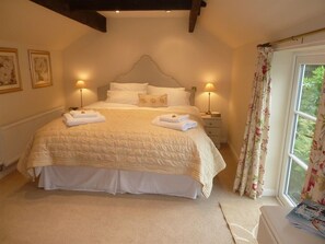 A neatly made bed with a quilted cover, two bedside lamps, and a window with floral curtains. - The Coach House (Stafford)