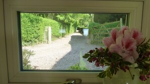 A window with a view of a gravel path leading to a gate, surrounded by greenery. - The Coach House (Stafford)