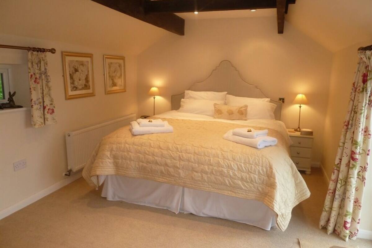 A bedroom with a large bed, two bedside lamps, a radiator, and a window with curtains.