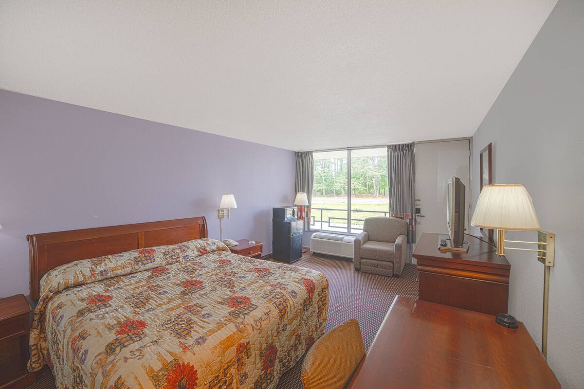 A hotel room with a large bed, a desk, a chair, a TV, and a window with curtains.