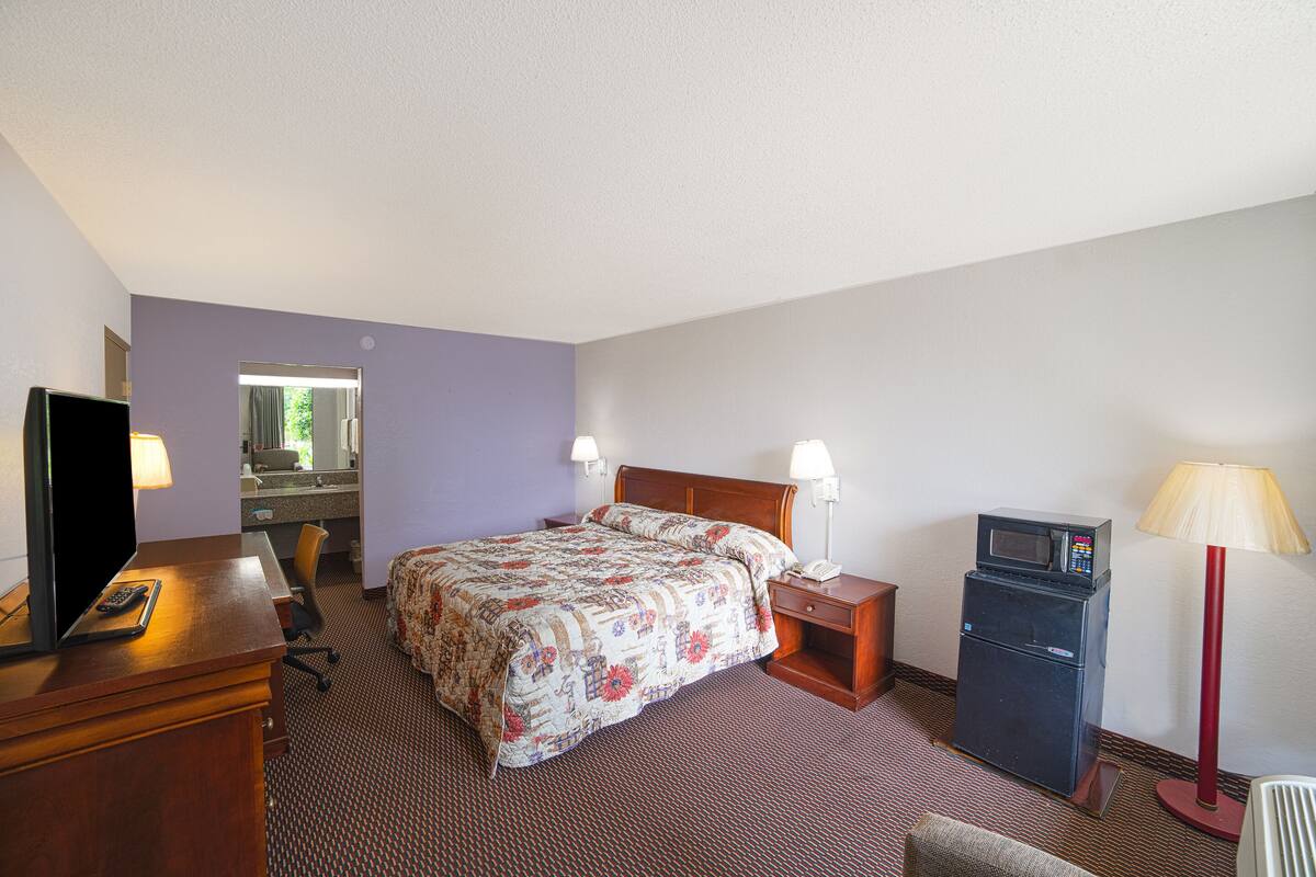A hotel room with a bed, bedside table, lamp, TV, and a microwave.