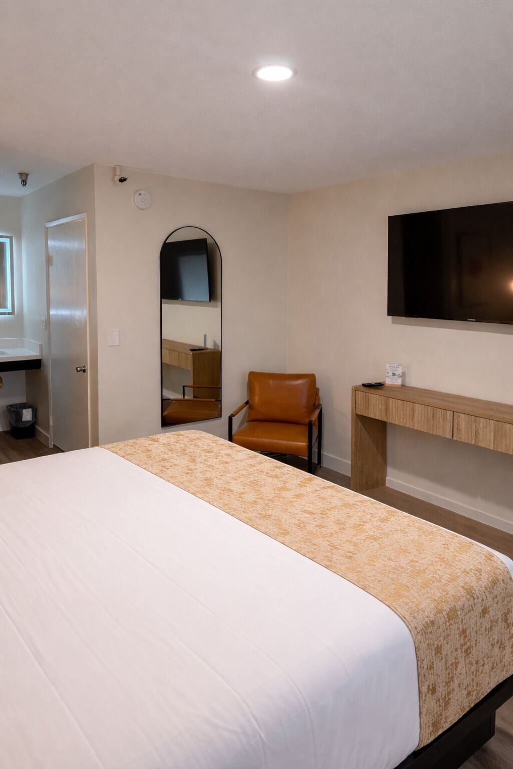 Une chambre d’hôtel équipée d’un lit, d’une chaise, d’un bureau, d’un miroir et d’un téléviseur fixé au mur.