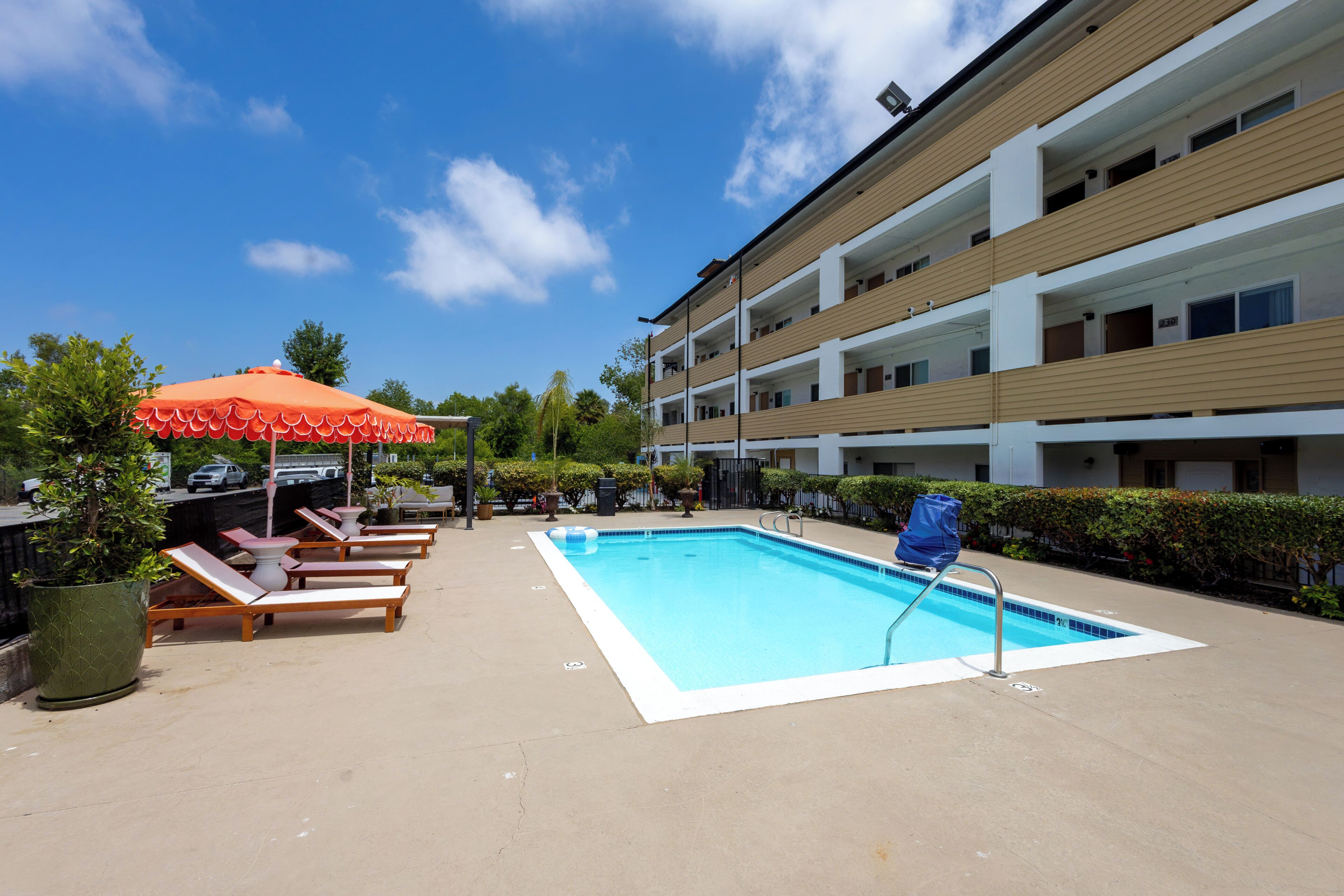 A swimming pool with lounge chairs and umbrellas, surrounded by a multi-story building.
