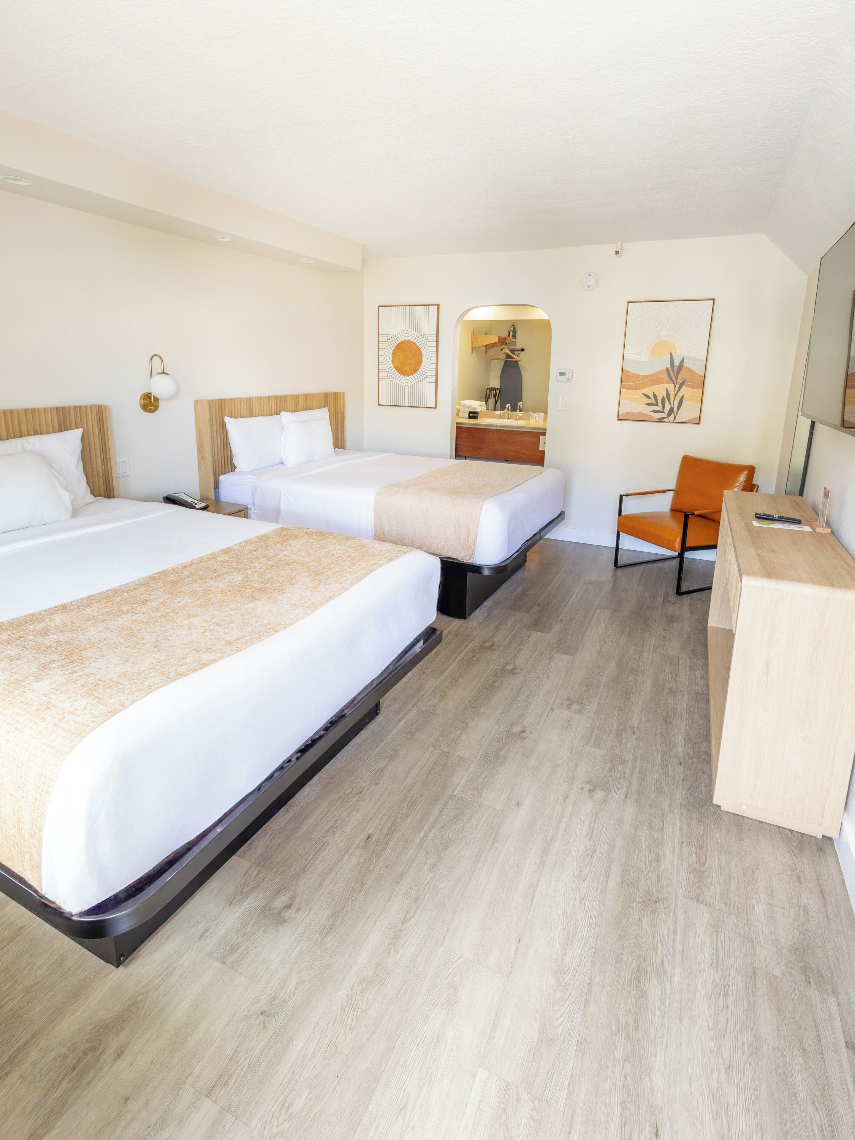 Ein Hotelzimmer mit drei Betten, einem Schreibtisch, einem Stuhl, einem Spiegel und Bildern an der Wand.