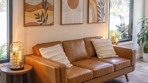 A brown leather sofa with two white pillows, a small round table with a candle, and three framed artworks on the wall. - The Alcala Hotel Mission Valley/Seaworld (San Diego)