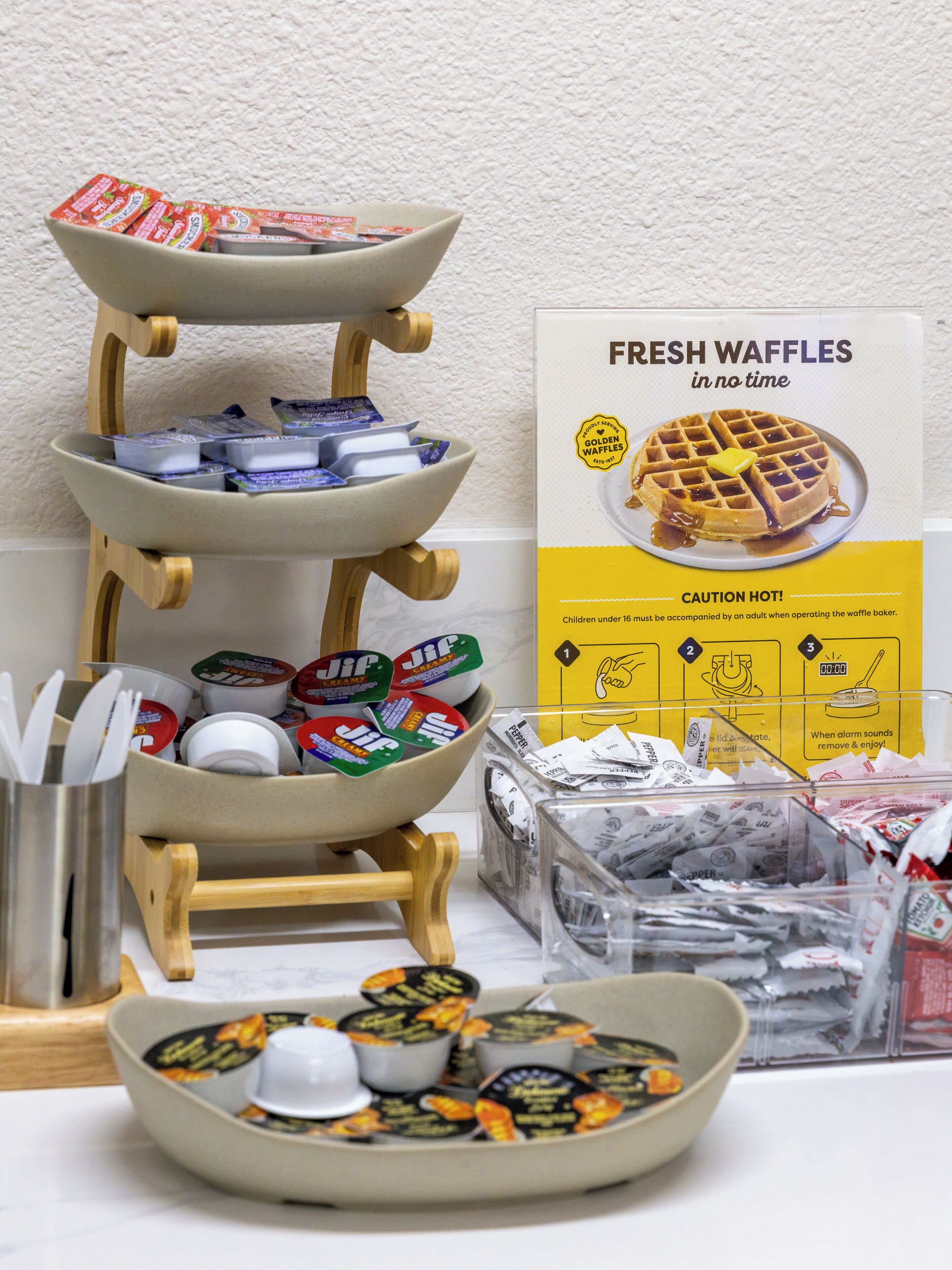 A waffle maker with instructions, a bowl of waffles, and various condiments.