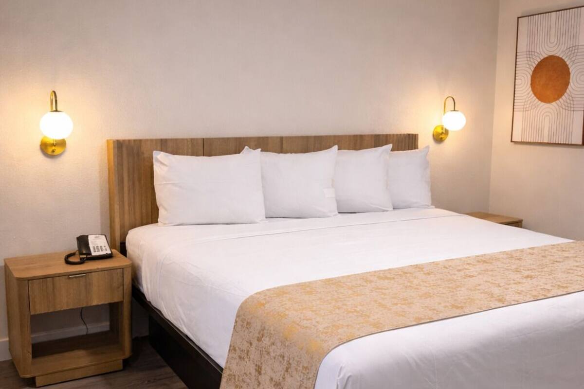 A hotel room with a large bed, bedside tables, and wall-mounted lighting.