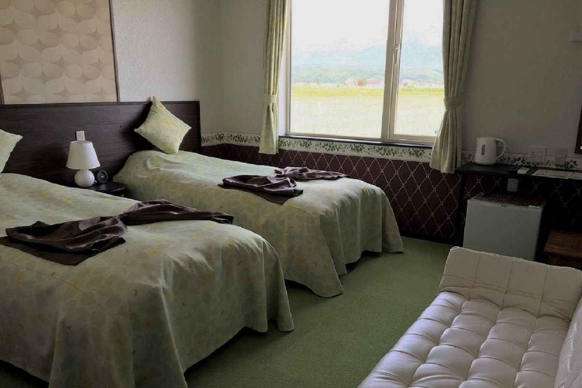 Habitación de hotel con dos camas, una kitchenette pequeña y vistas al campo.