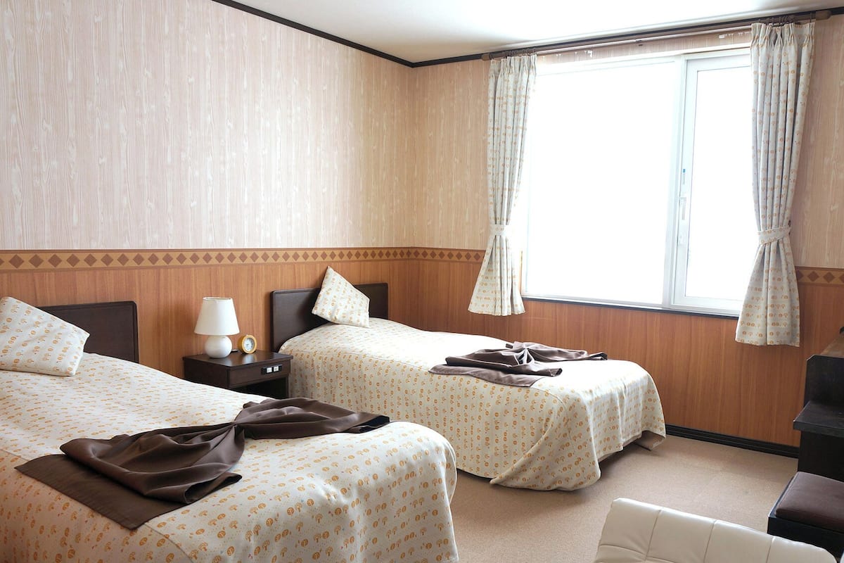 Une chambre d’hôtel avec deux lits, une télévision, un bureau et une fenêtre avec des rideaux.