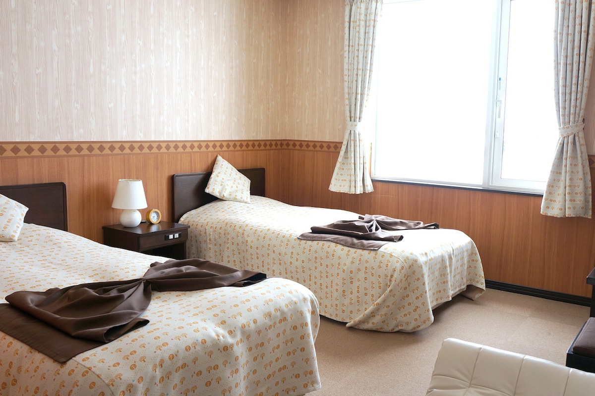 Habitación de hotel con dos camas, televisión, escritorio y ventana con cortinas.