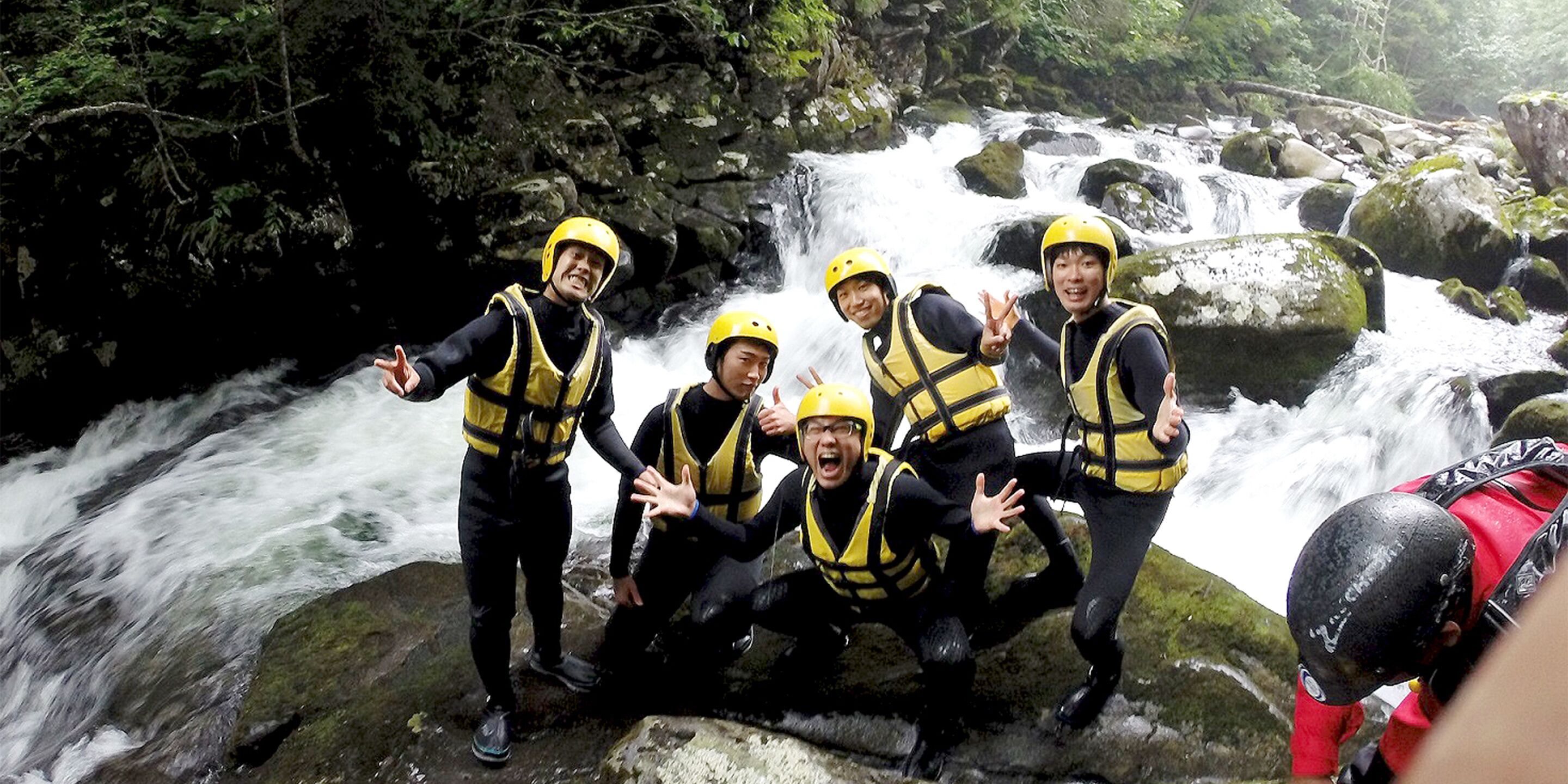 A group of people in yellow helmets and life vests posing by a waterfall.