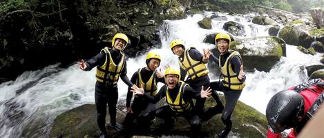 A group of people in yellow helmets and life vests posing by a waterfall.