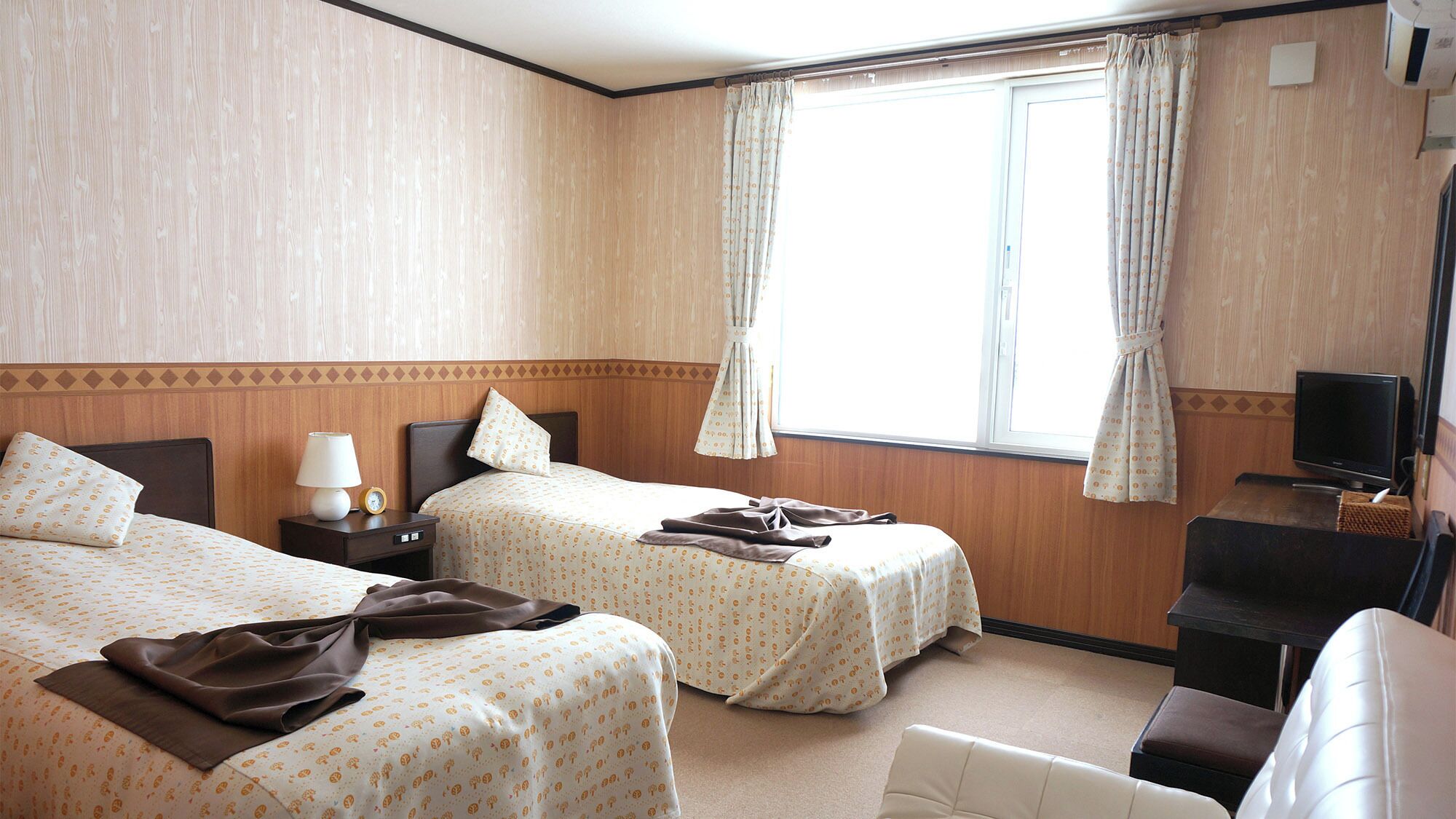 Une chambre d’hôtel avec deux lits, une télévision, un bureau et une fenêtre avec des rideaux.