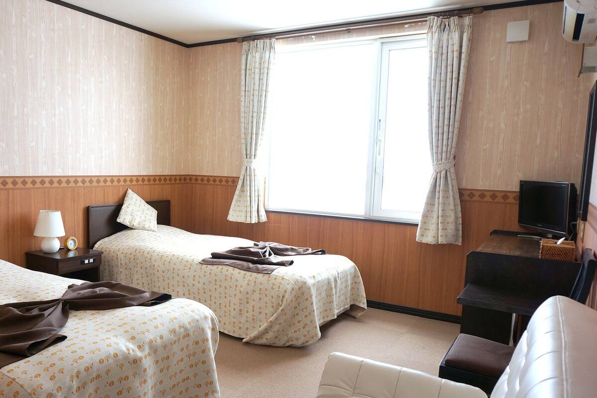 Une chambre d’hôtel avec deux lits, une télévision et une fenêtre avec des rideaux.