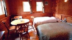 A cabin with a wooden interior, a round table, two beds, and a window. - Petit Hotel Gracey Tomamu (Shimukappu)