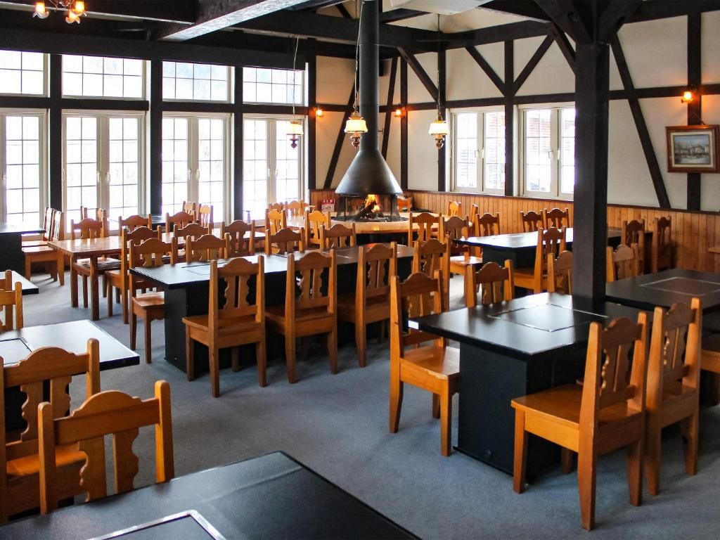En restaurantindretning med flere borde og stole, store vinduer og en central pejs.