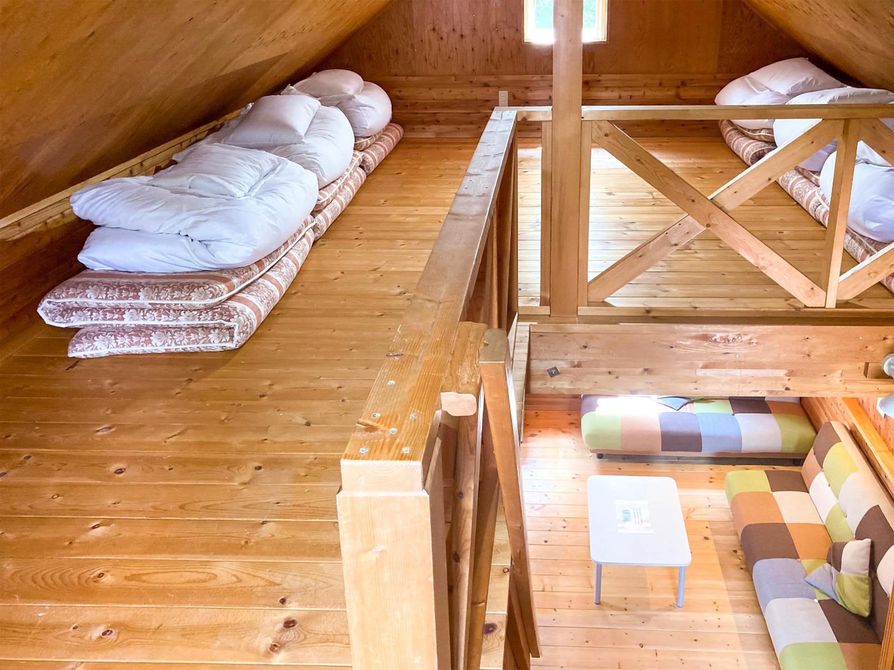 Un acogedor dormitorio en el ático con piso de madera, cama con ropa blanca, sofá con cojines estampados y una mesita.