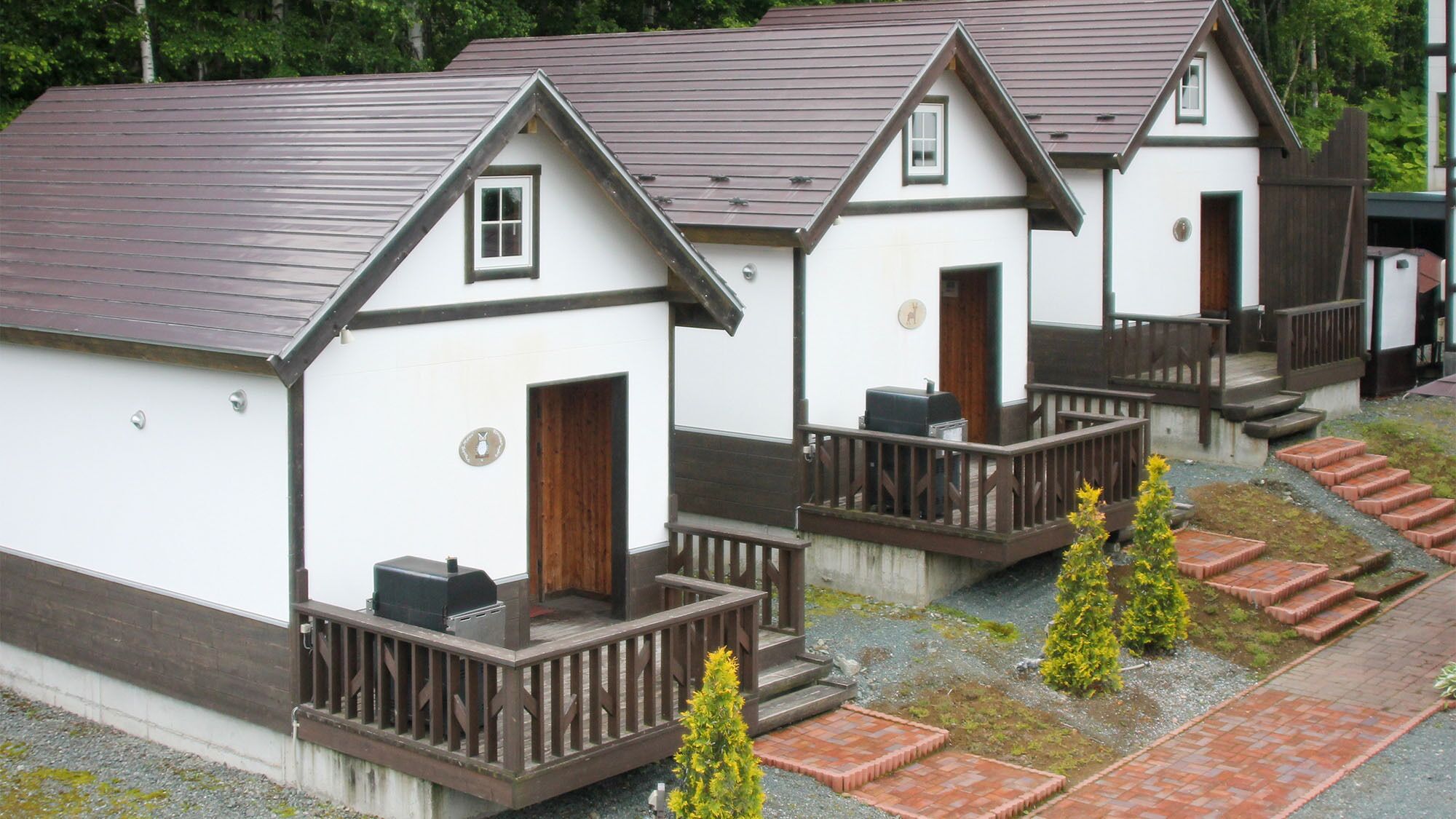 Eine Reihe kleiner, weißer Holzhütten mit braunen Dächern und Holzbalkonen, jeweils mit einer Tür und einem Fenster.
